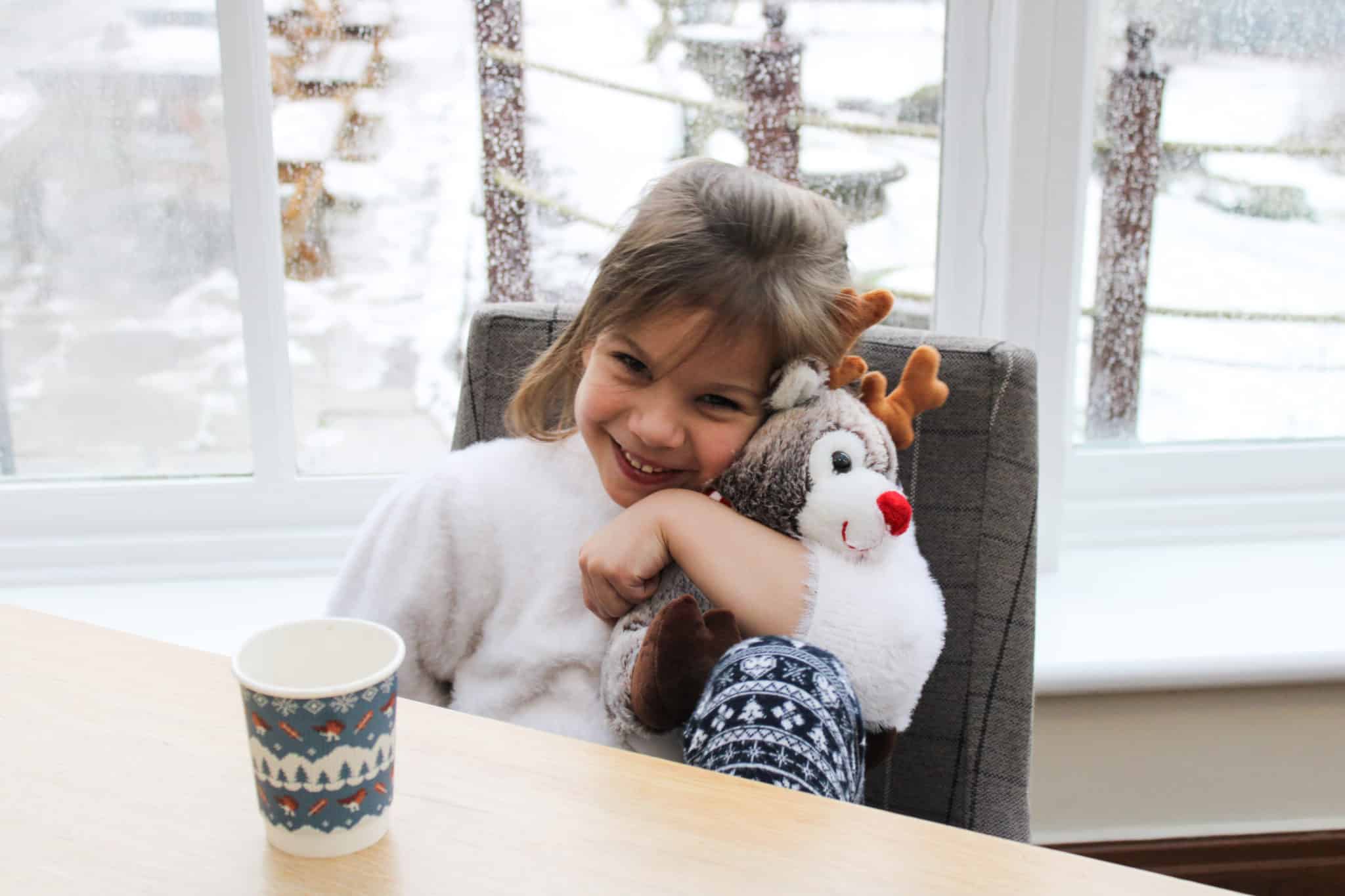 Girl sitting at a table and hugging a reindeer plushie