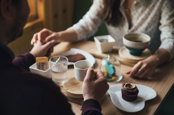 Two People Holding Hands while having coffee and cakes