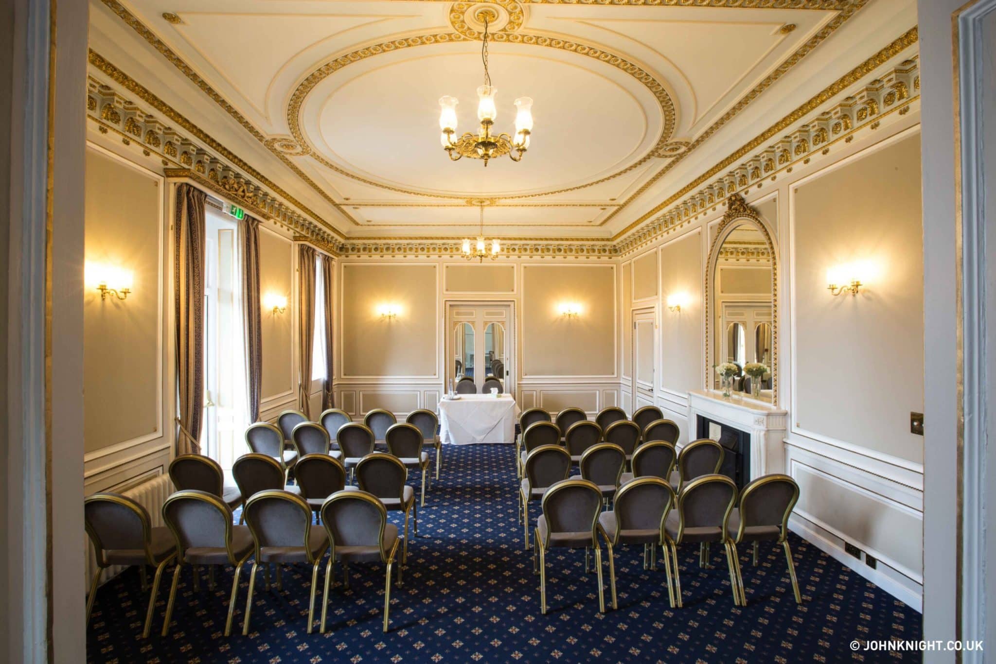 Room with four rows of chairs facing a table with two chairs behind it