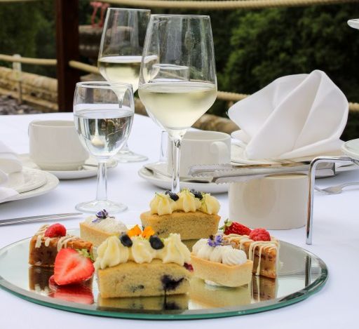 Two wine glasses, tea cups and a plate of pastries with a strawberry