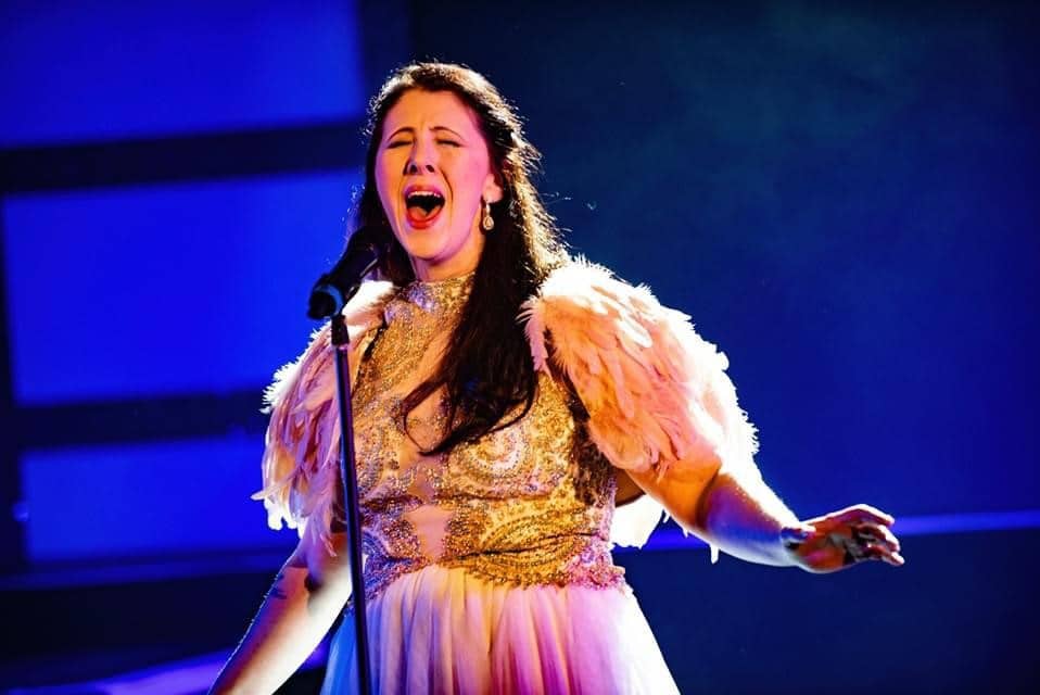 Woman wearing a white dress with feathered shoulder pads singing