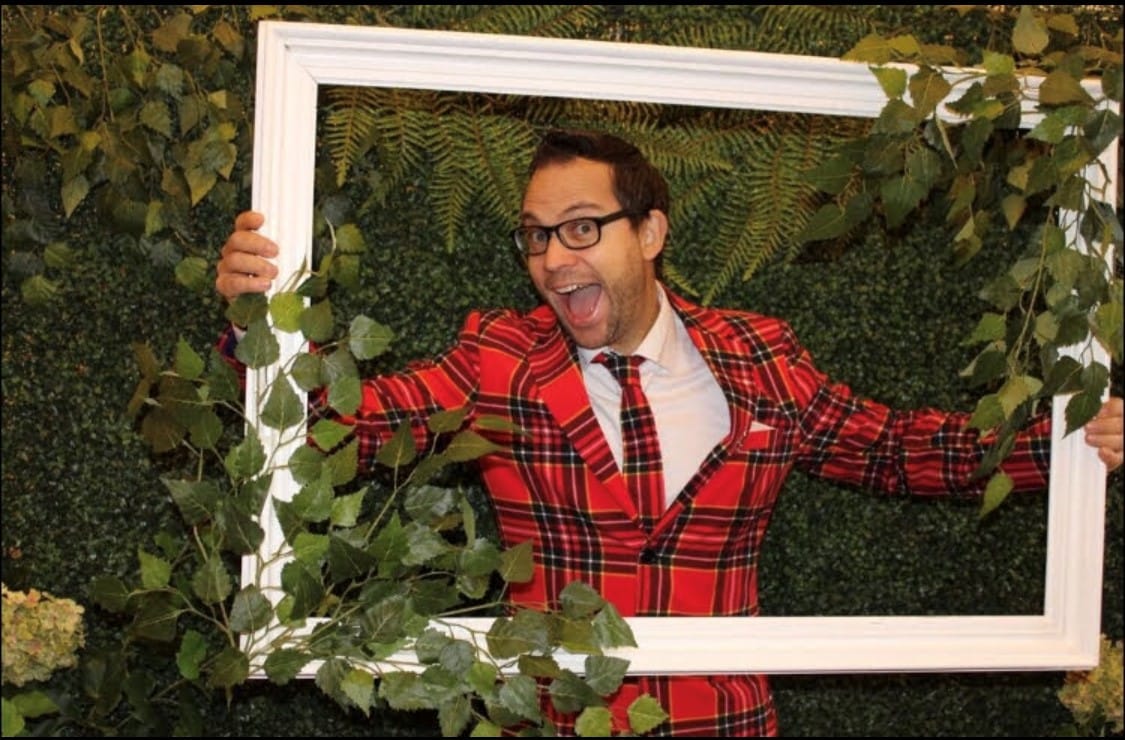 Man with red and black shirt and tie posing inside a large white frame