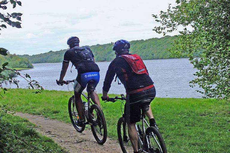 Two people cycling next to a lake