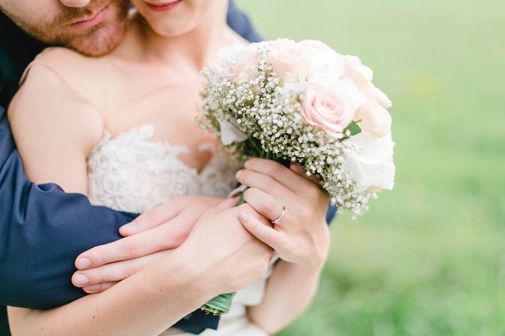 Man hugging woman in wedding dress holding a flower bouquet