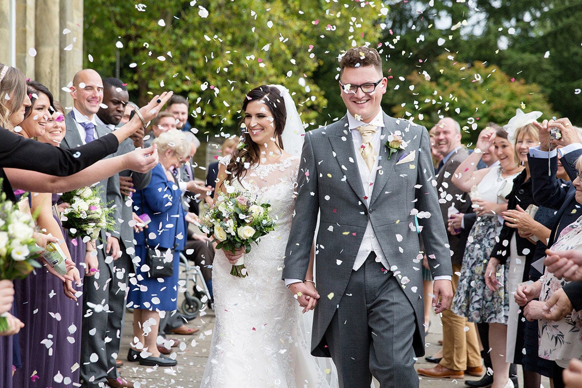 Just married coupe walking as confetti is being thrown at them by the surrounding people.