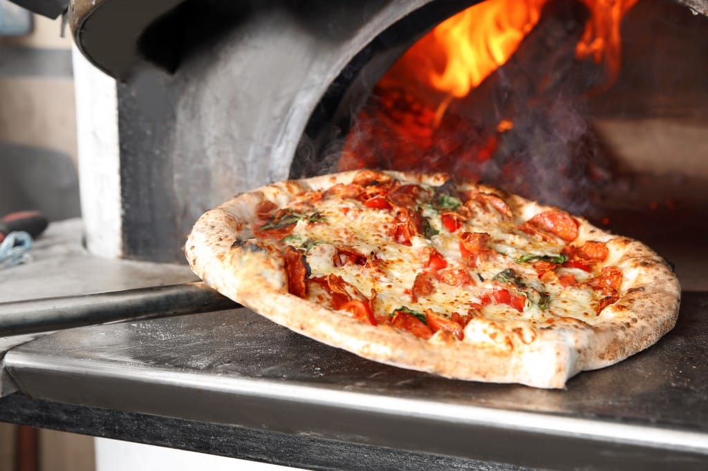 Pizza being taken out of a pizza oven