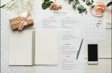 Wedding Planning checklist with some flowers, wedding rings, mobile phone, notebook and candle around it