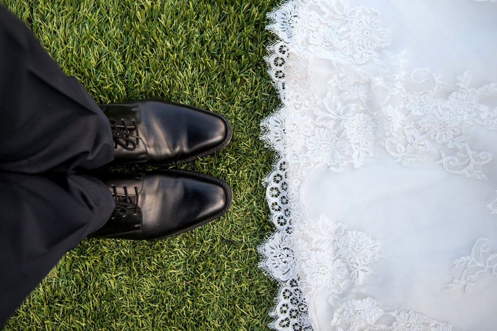 Black dress shoes and bottom of a white wedding dress