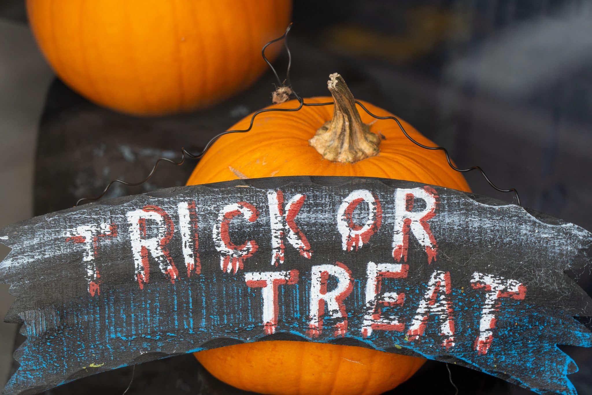 Black banner with "trick or treat" written on it, in front of two pumpkins