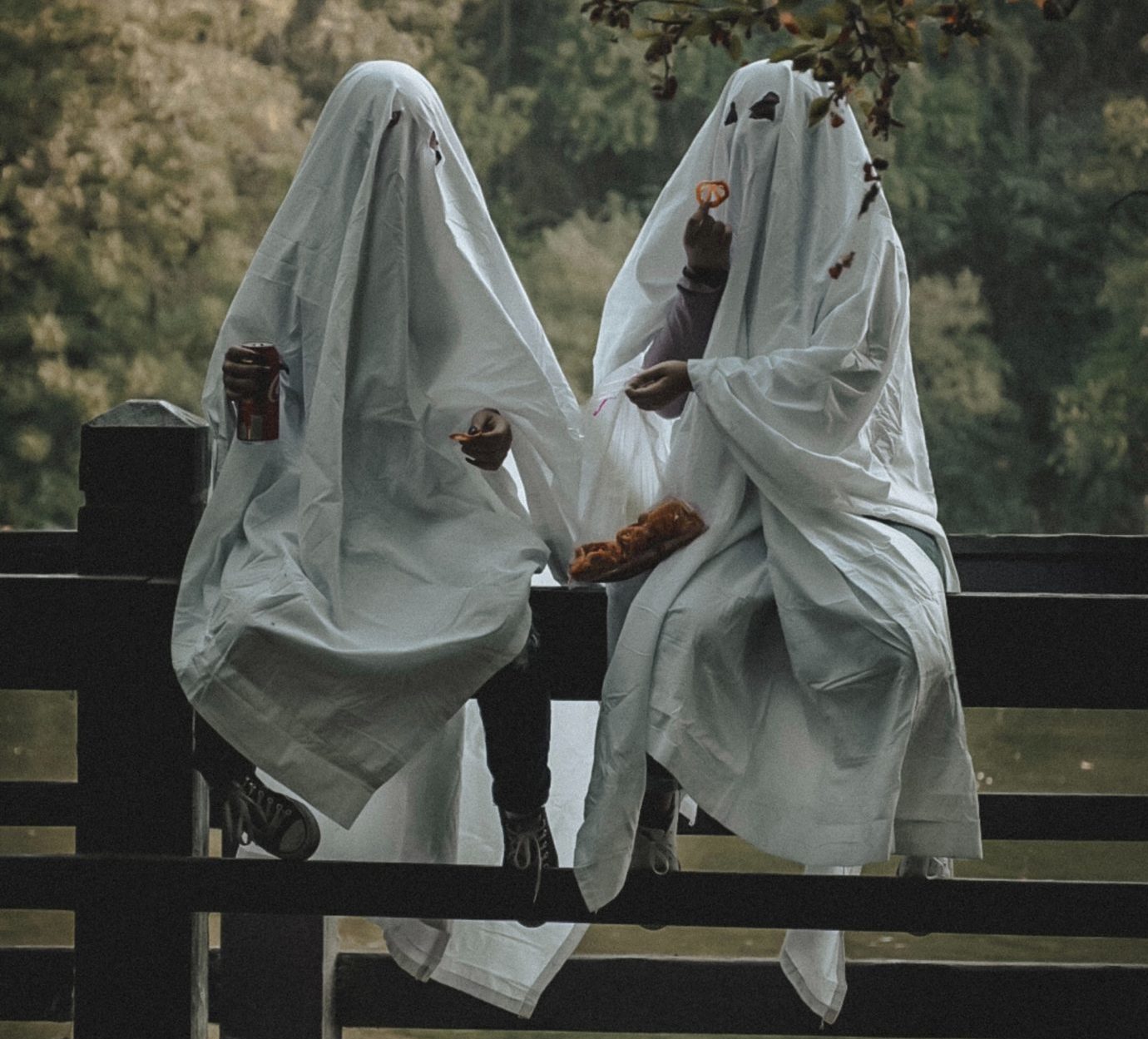 Two kids dressed as ghosts eating snacks from a bag