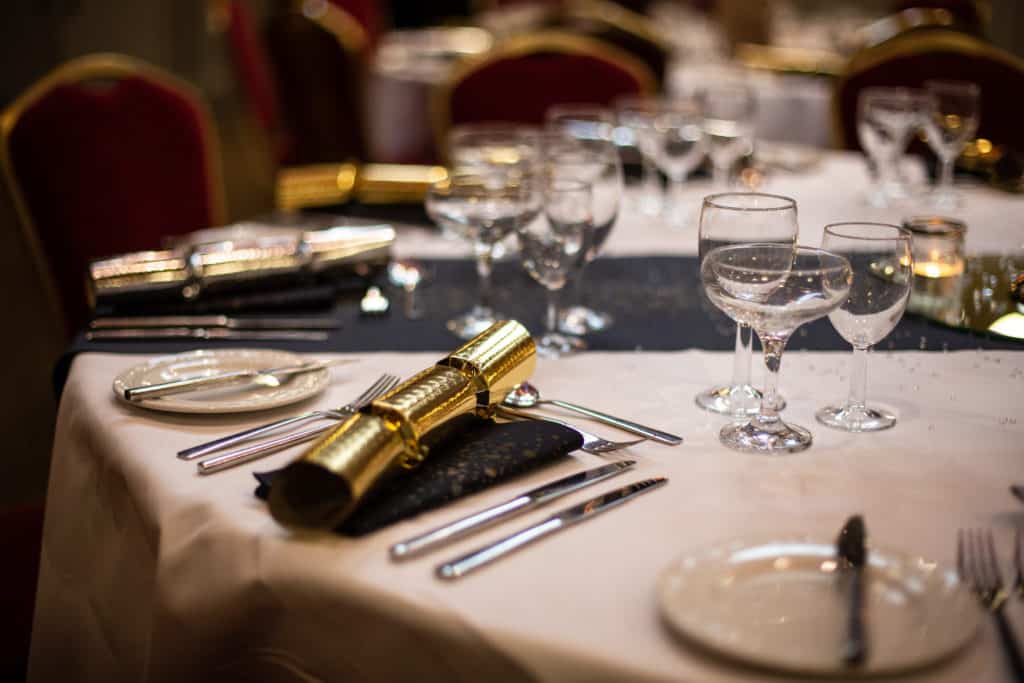 tables dressed for a Christmas party with glasses, plates, cutlery and gold Christmas crackers