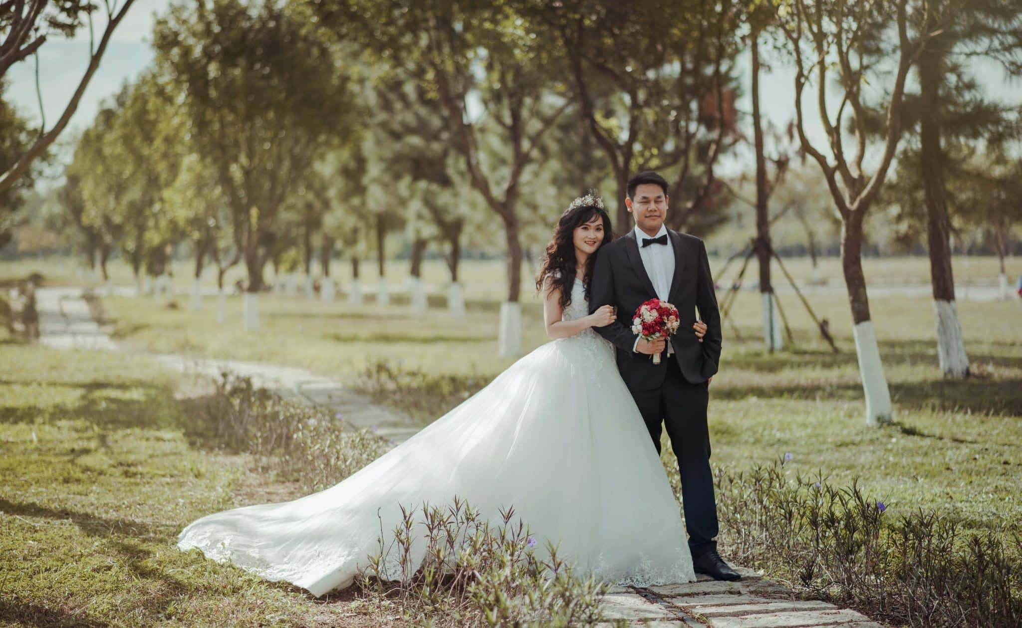 married couple in a suit and a dress stand together in a garden of trees