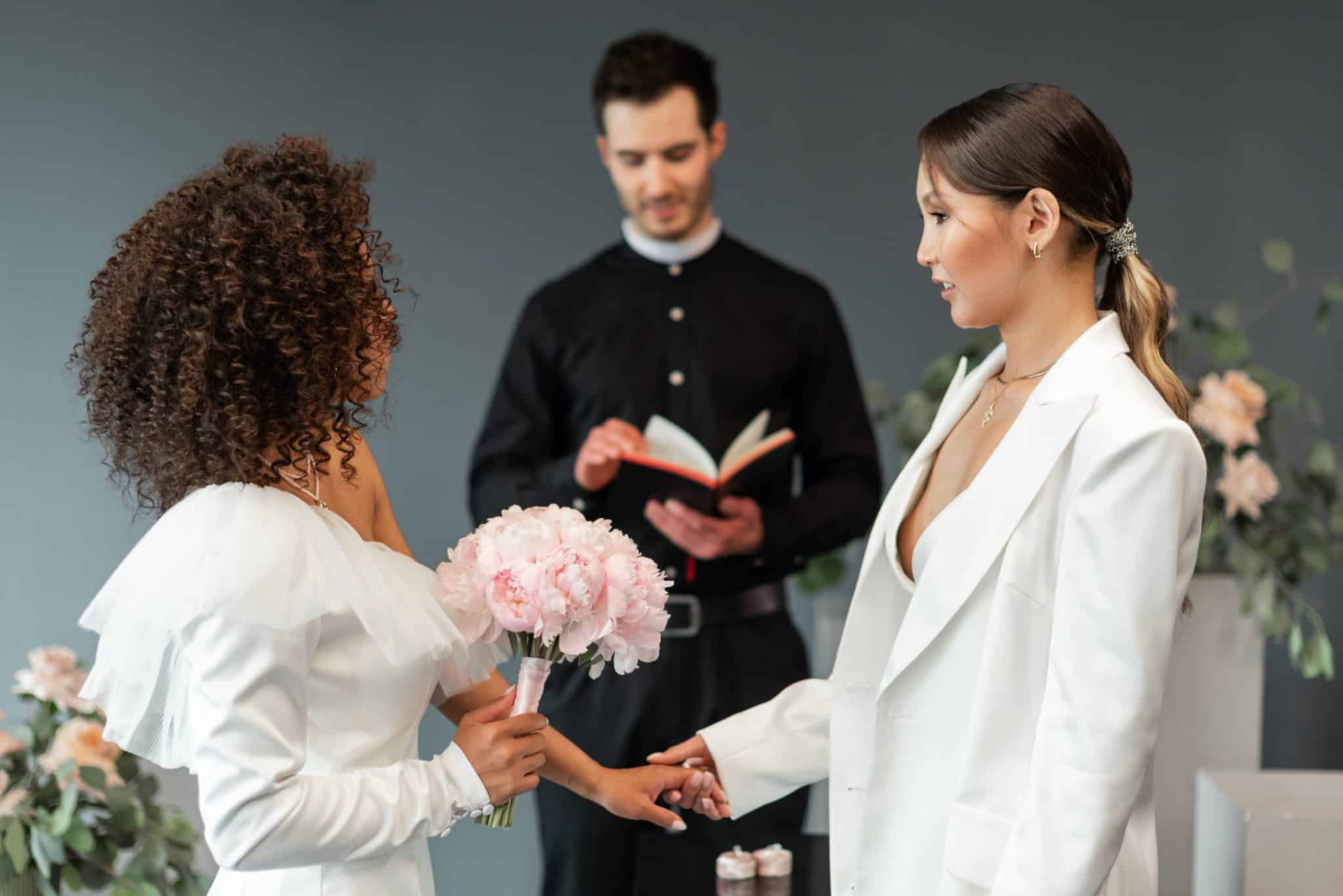 two women stand at the alter, one in a dress, the other in a bridal suit