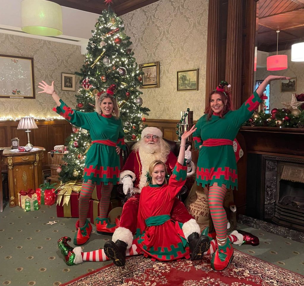 Santa and three Elves in front of a Christmas tree