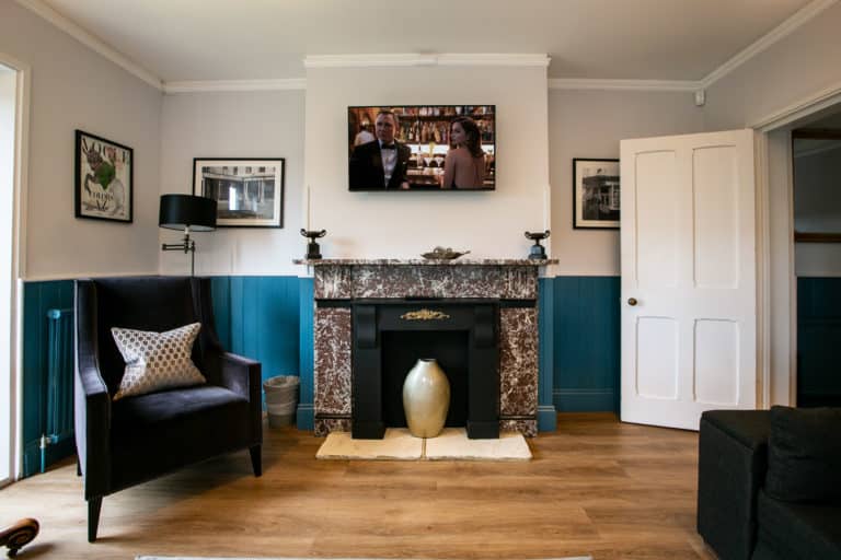 Living room with armchair, chimney with a vase in it and a tv playing a movie with Daniel craig