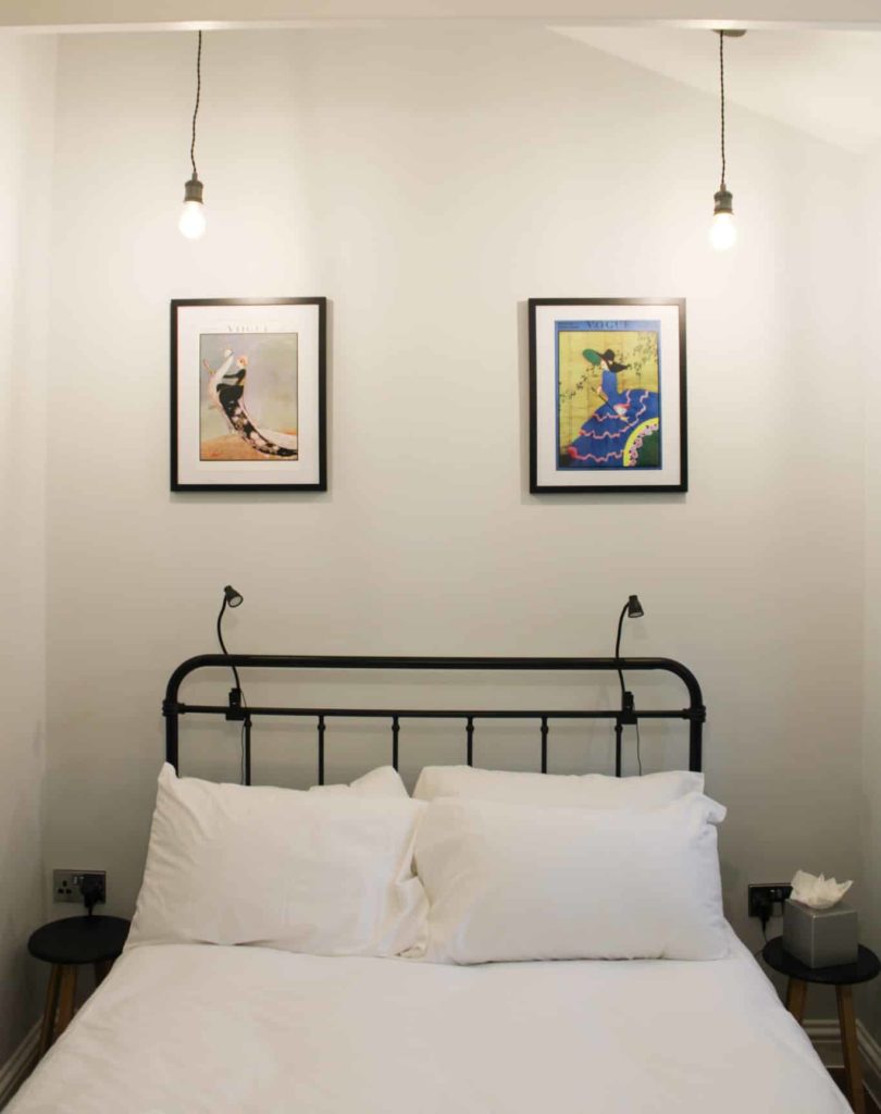 double bed with drop down lighting and framed canvases on the wall