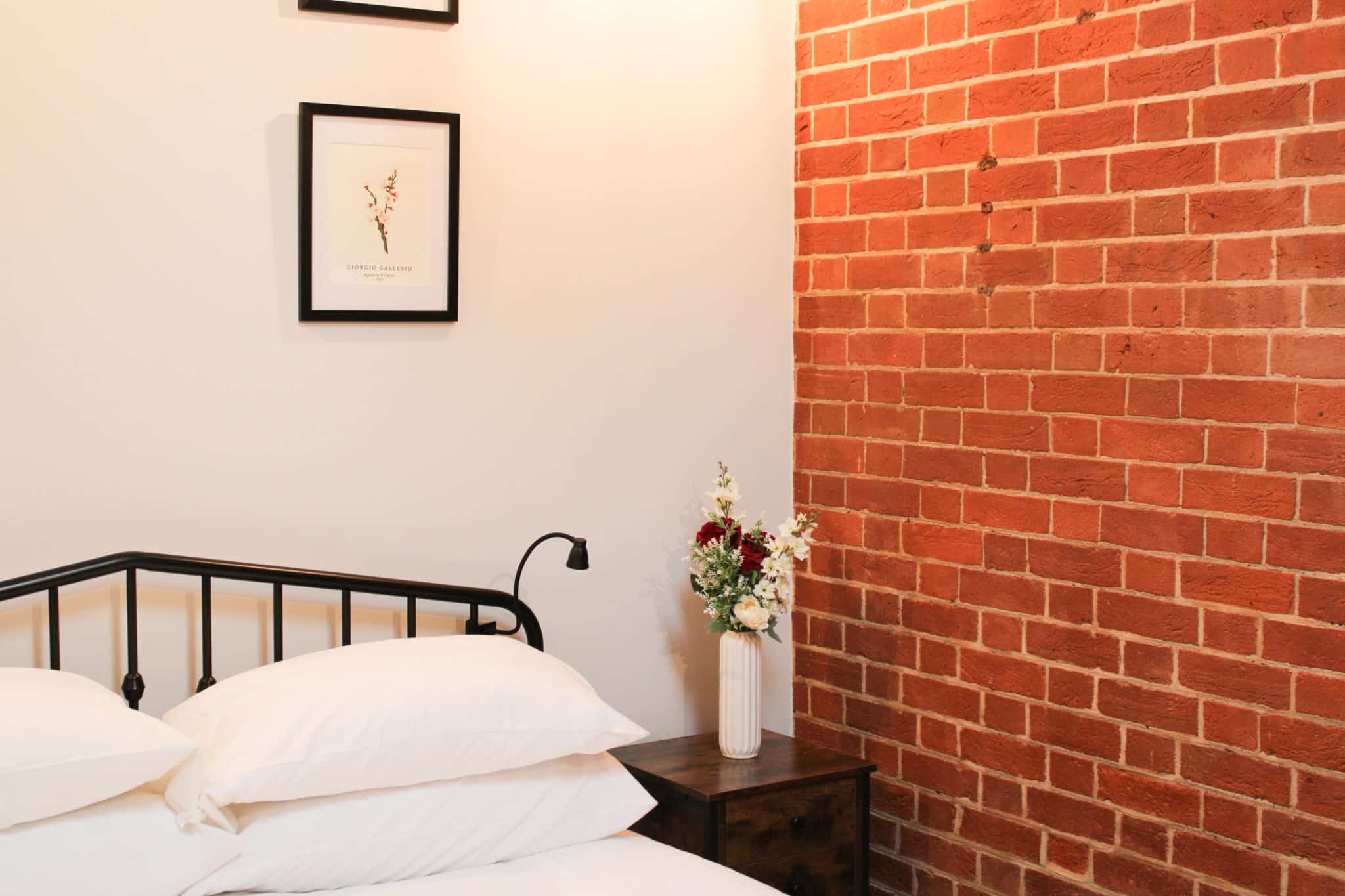 Flower Arrangement on a night table next to a bed and brick wall