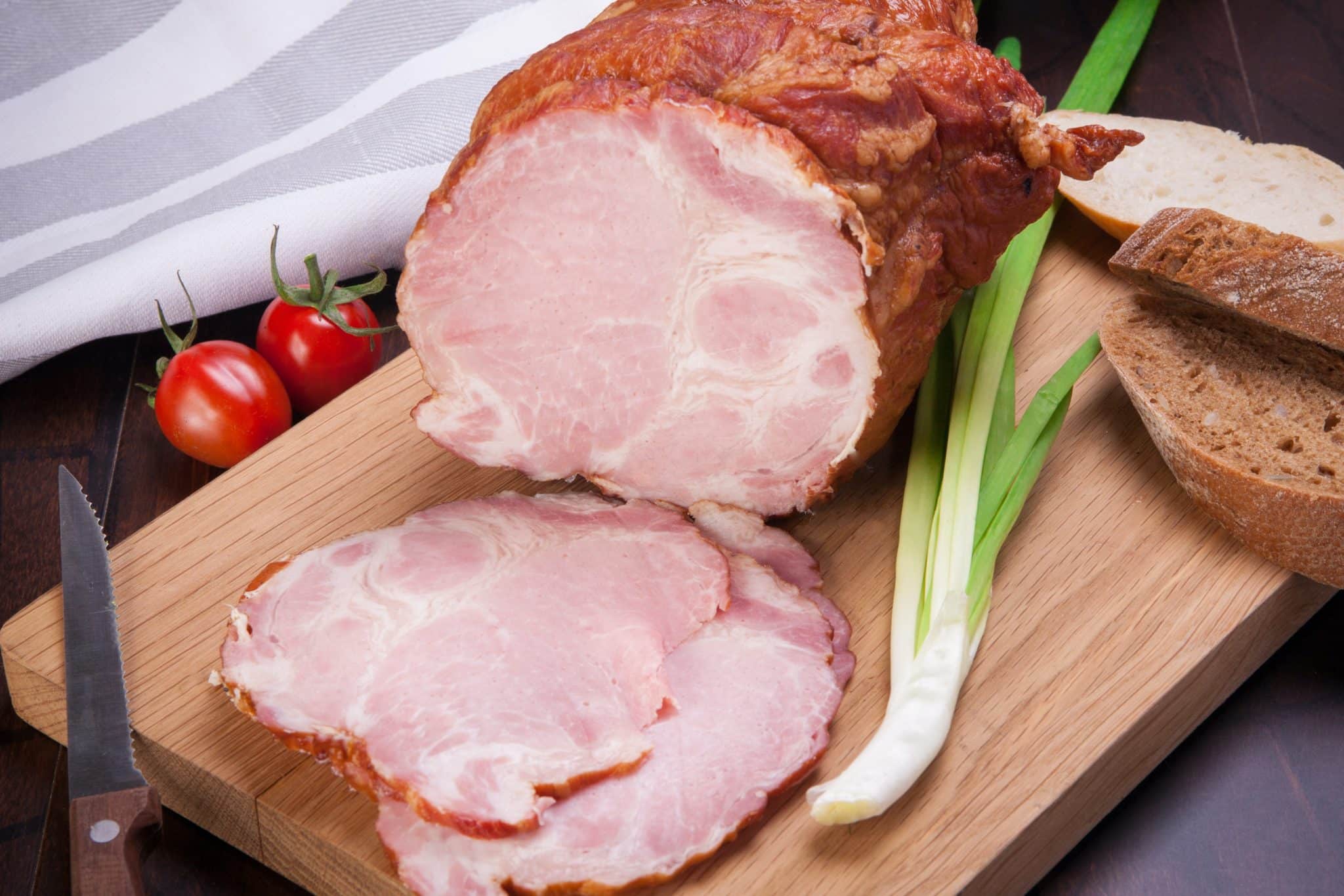 joint of cooked ham resting on chopping board with leeks and tomatoes