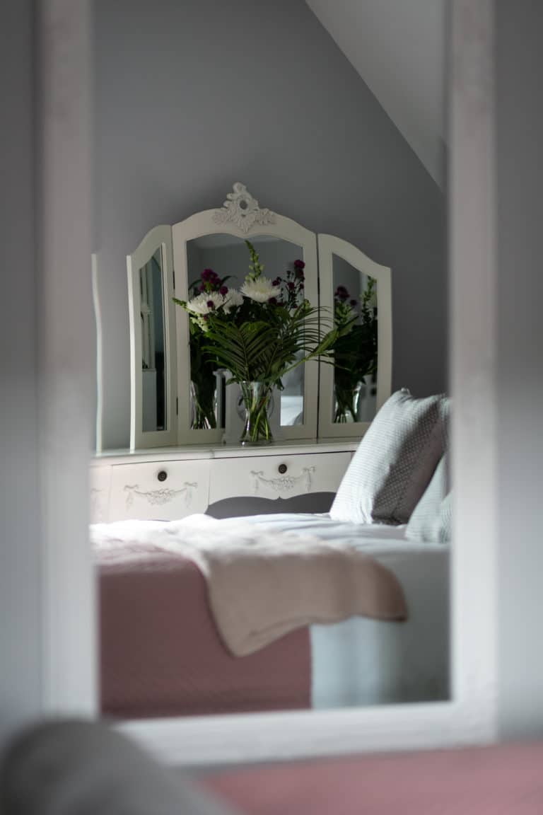 Mirror reflecting a bed and a table with drawers