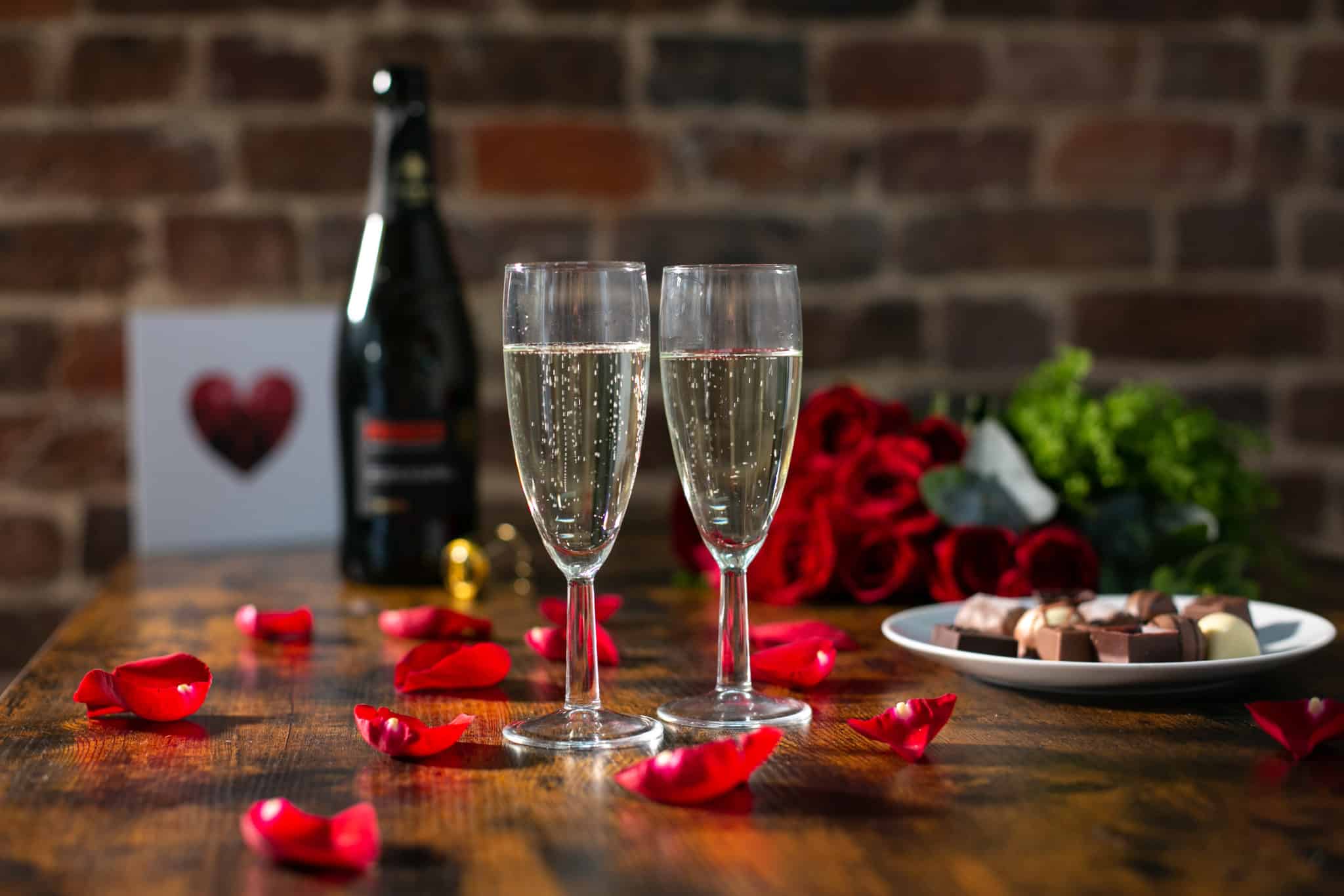 Valentines day themed table with two glasses of wine, chocolates and roses