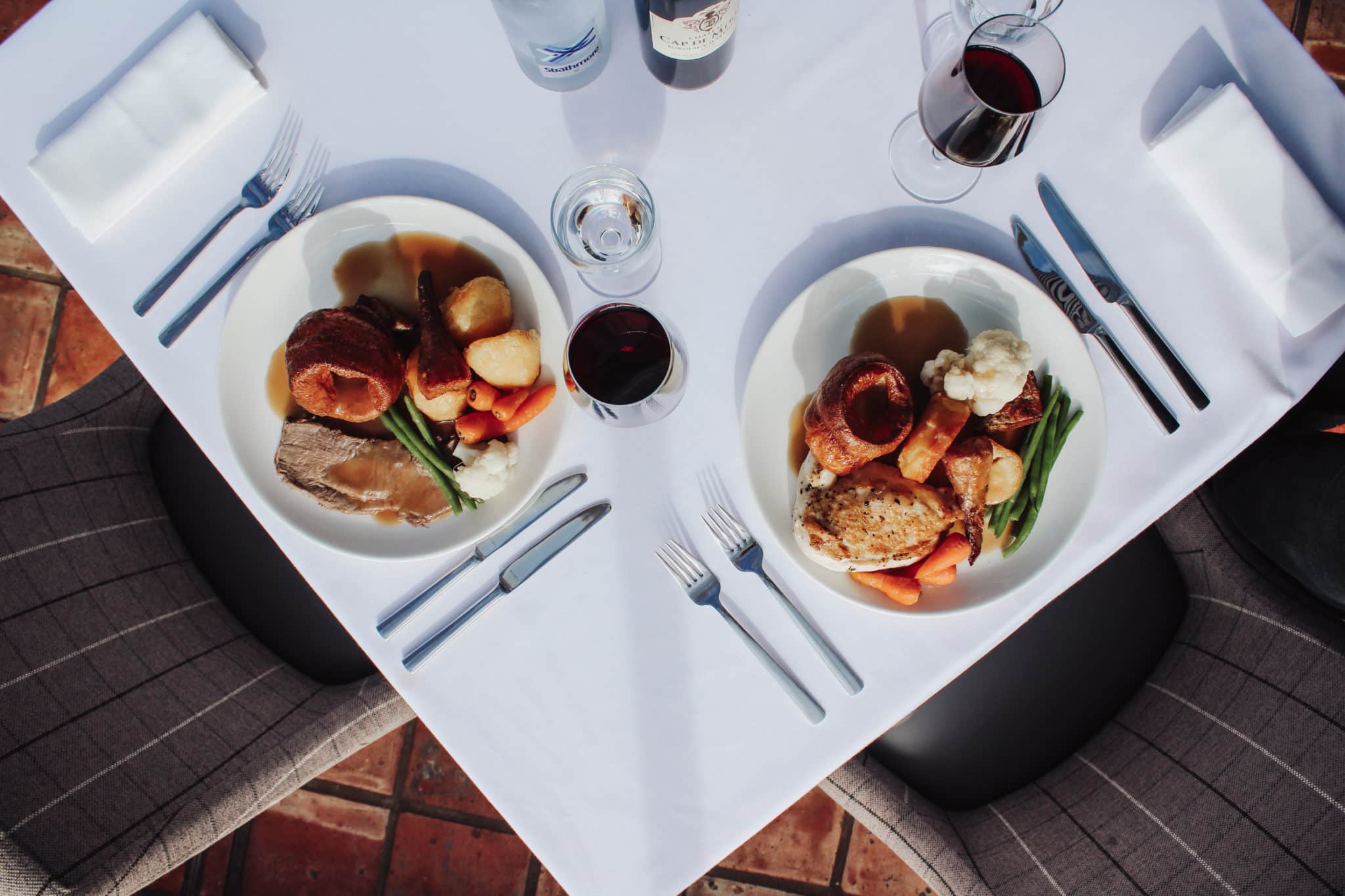 Two servings of sunday roast with two glasses of red wine